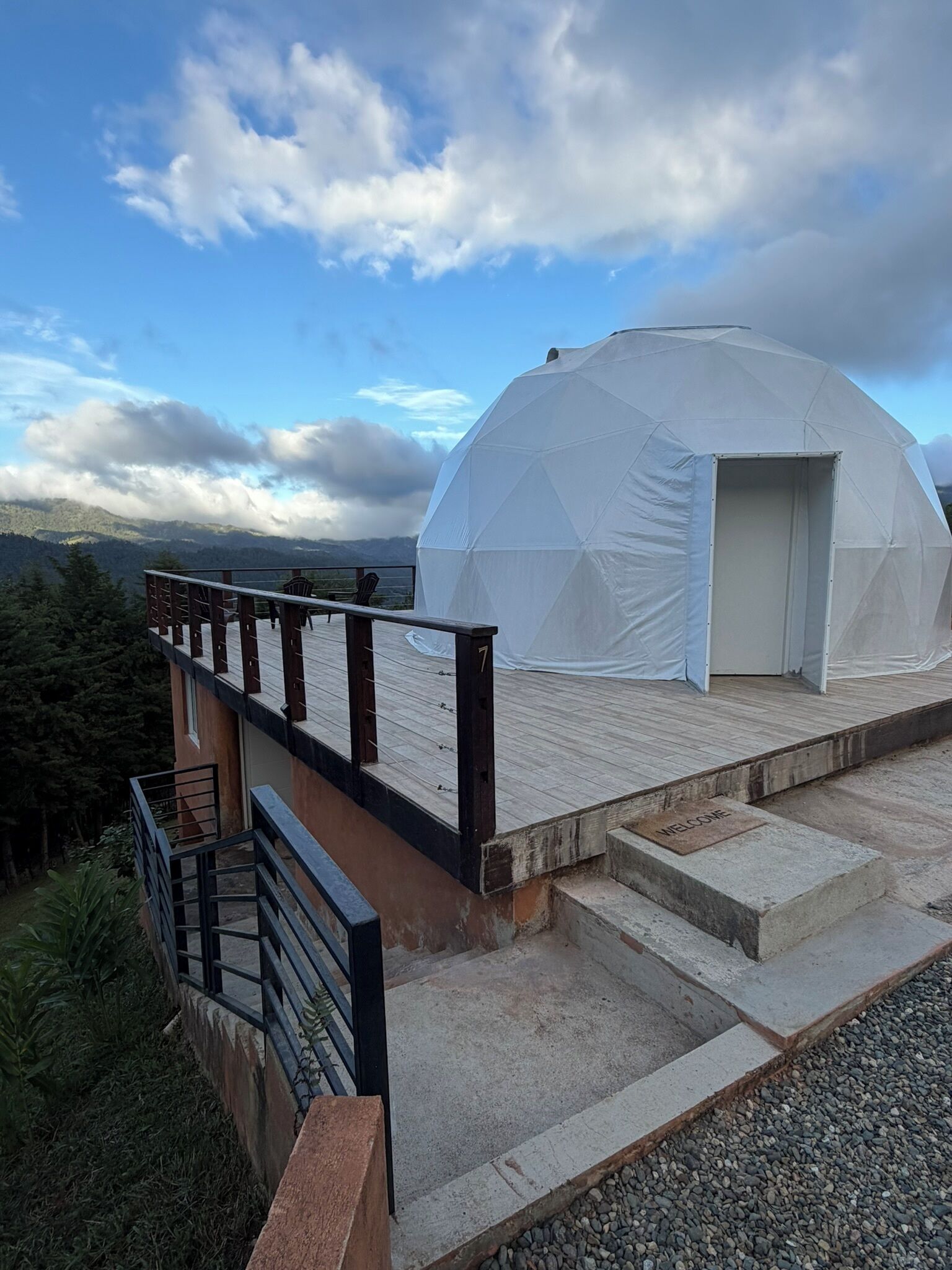 A dome-shaped tent with a wooden deck and a metal railing, overlooking a mountainous landscape.