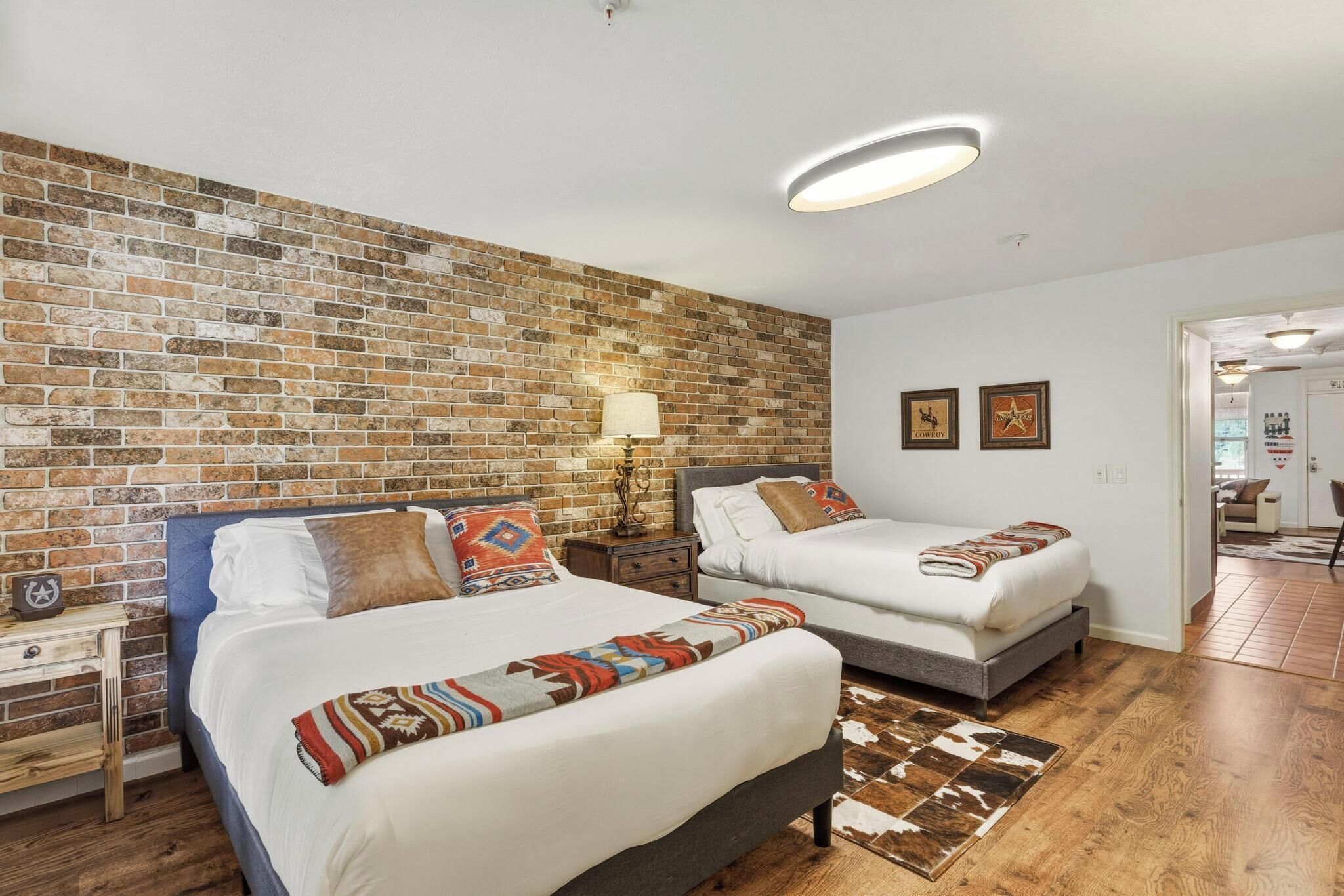 A hotel room with two beds, a brick wall, a ceiling light, and a door leading to another room.