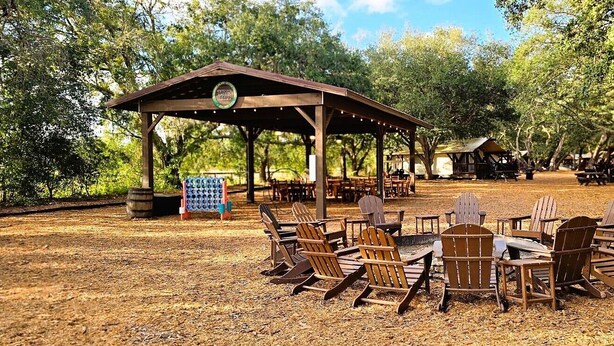 A covered outdoor seating area with Adirondack chairs and tables, surrounded by trees. - River Ranch  Oasis /  Wild West Escape (River Ranch)