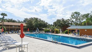 A swimming pool with lounge chairs and umbrellas, surrounded by trees and a building. - River Ranch  Oasis /  Wild West Escape (River Ranch)