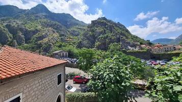 Un edificio de piedra con techo de tejas, un estacionamiento y montañas al fondo.
