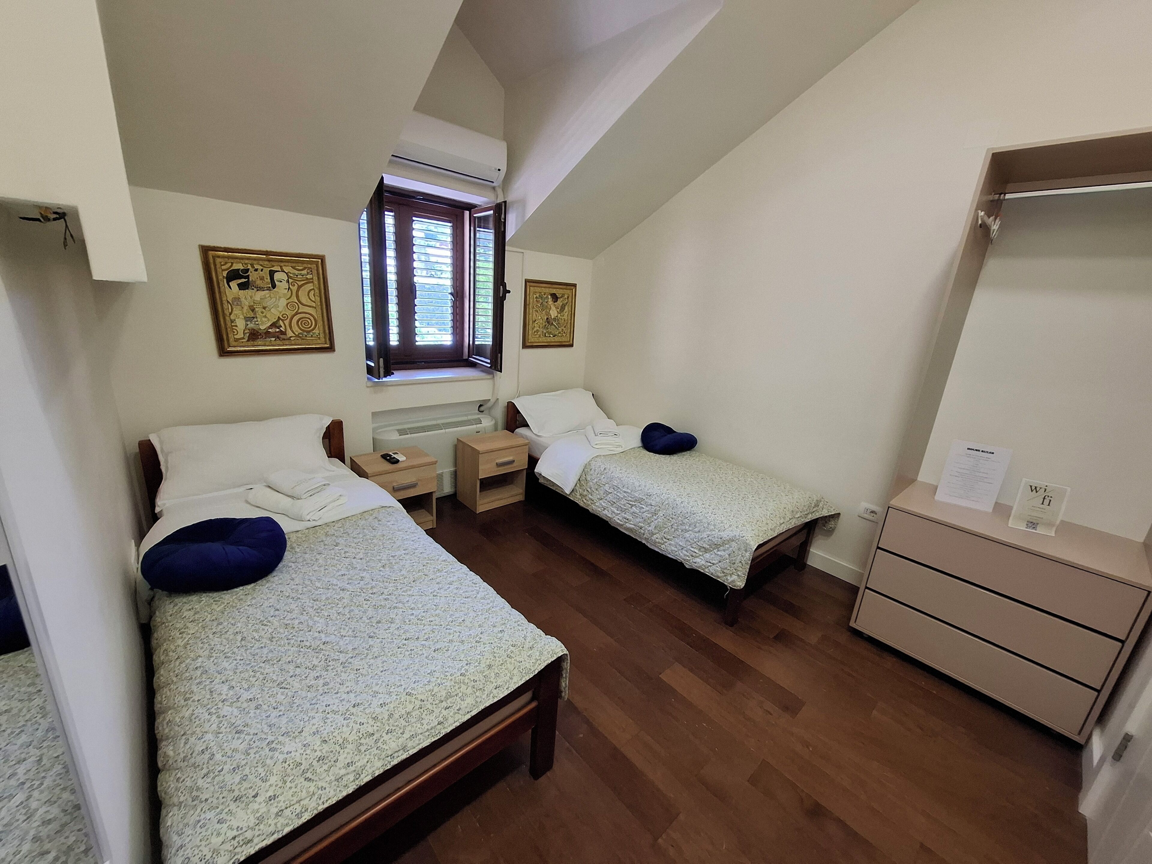 Una habitación con dos camas, un calentador, una ventana con persianas, un espejo y un armario pequeño.