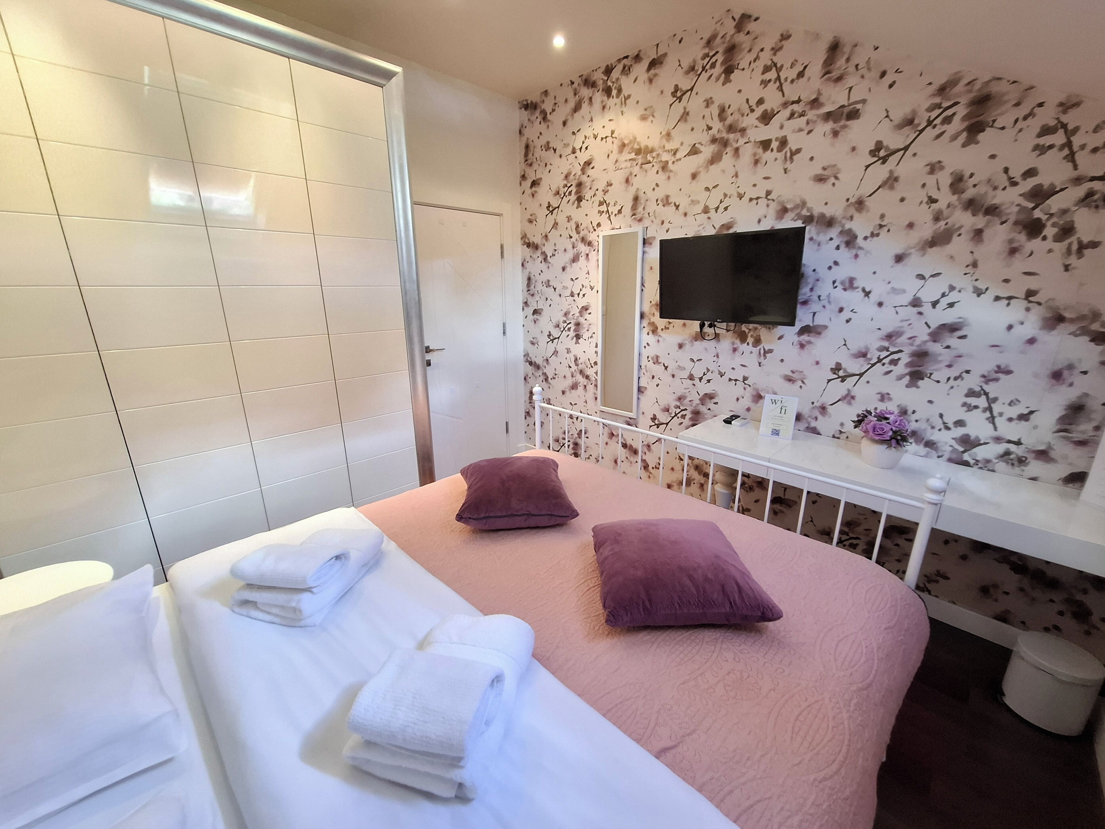 Habitación de hotel con dos camas, televisión, un papel tapiz floral y un inodoro blanco.