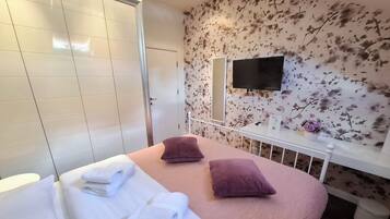 Habitación de hotel con dos camas, televisión, un papel tapiz floral y un inodoro blanco.