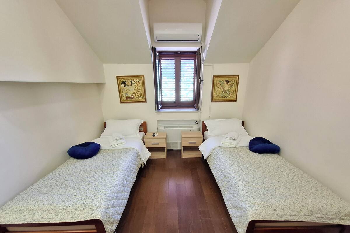 A twin room with two single beds, a small window, and a wall-mounted air conditioner.