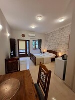Habitación de hotel compacta con cama, escritorio, silla, mesita y kitchenette.