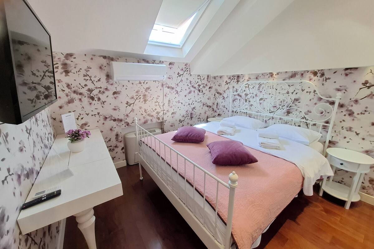 A bedroom with a bed, bedside tables, a desk, a chair, a TV, and a window.