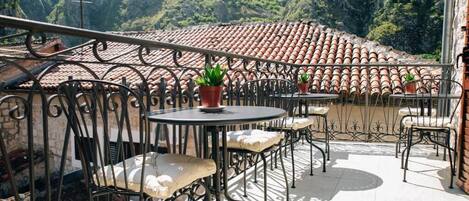 Terraza con mobiliario exterior, plantas en macetas y vistas a un tejado de tejas de arcilla y vegetación circundante.