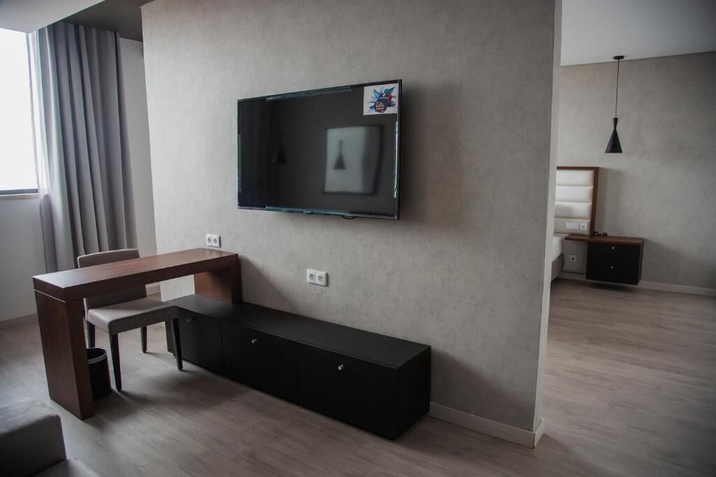 Una sala moderna con un televisor de pantalla plana montado en la pared, una mesa de comedor de madera y un banco negro.