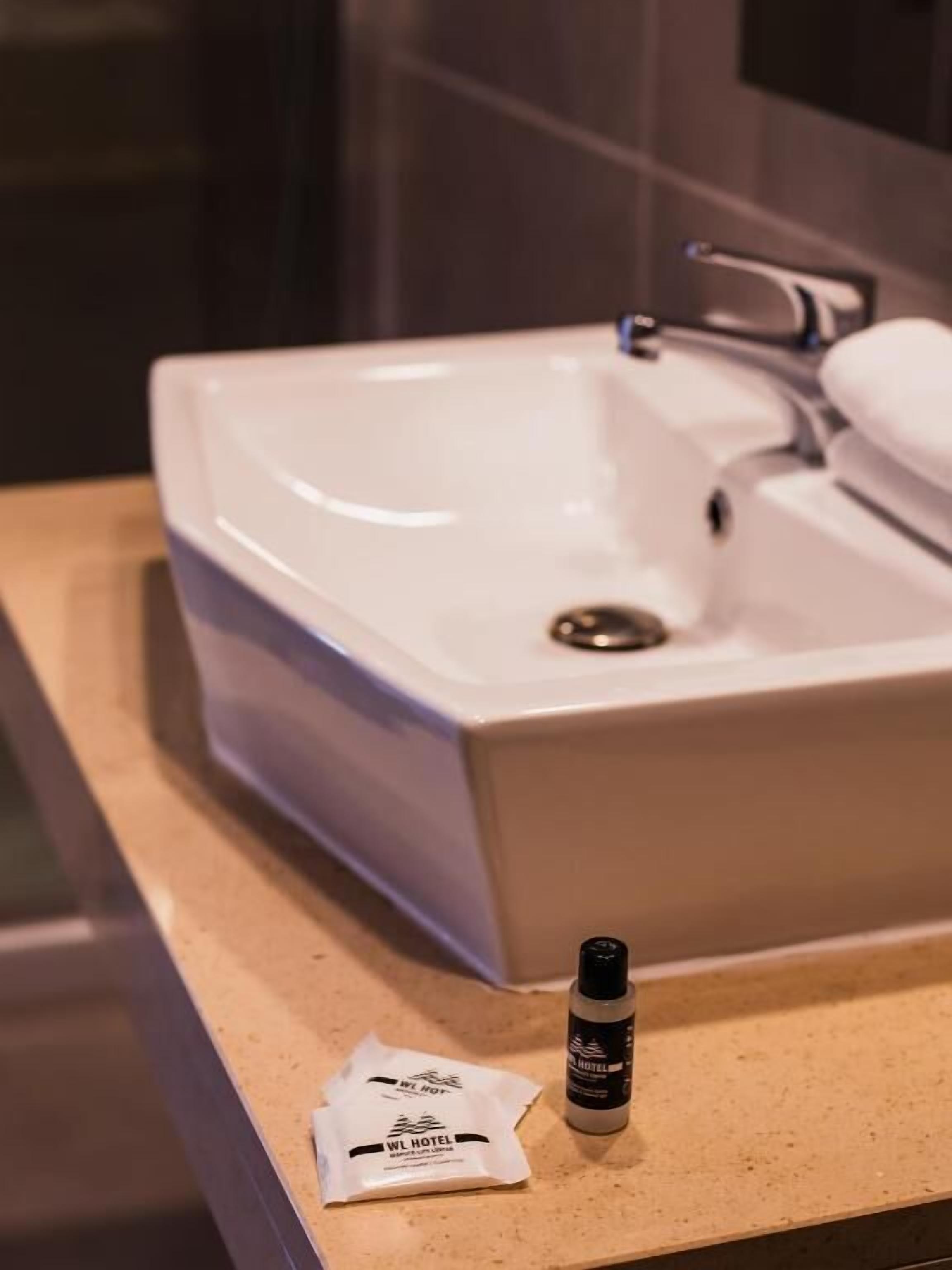 A bathroom sink with a white basin and a modern faucet. A bottle and a packet are placed on the countertop.