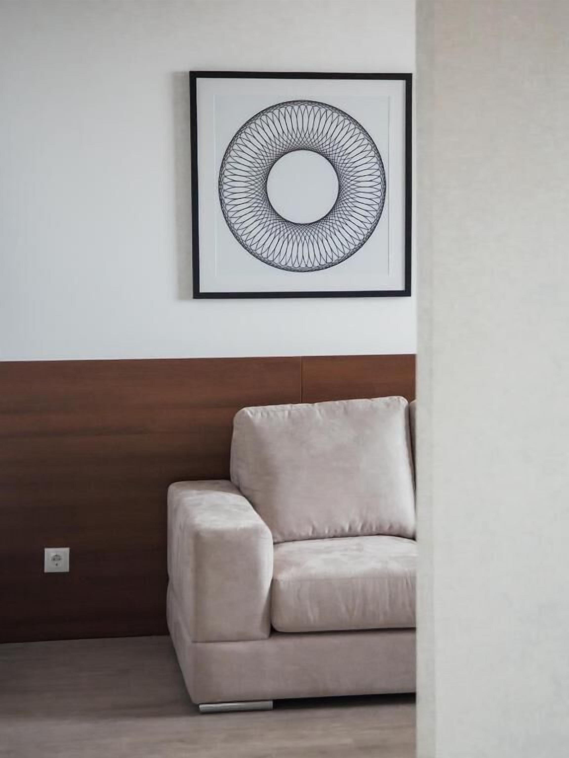 Una obra de arte abstracta enmarcada en una pared blanca sobre un sofá beige con cabecera de madera.