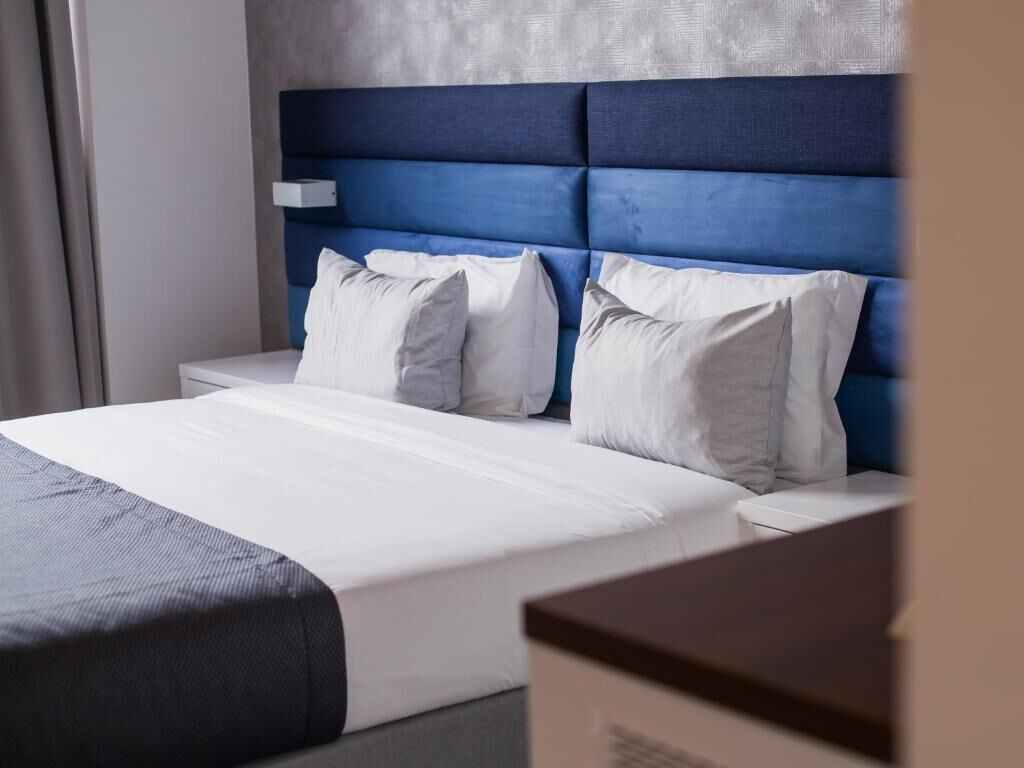 Een hotelkamer met een bed, witte beddengoed en een blauw hoofdeinde.