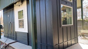 A house with a dark exterior, a white front door, and a window. - Tiny Blanco Retreat - River Tiny Home ~ Hill Country (Wimberley)