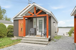 A small cabin with a porch, steps, and a view of a lake.