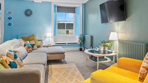 A modern living room with a sofa, armchairs, a coffee table, and a TV mounted on the wall. - Large House in Central Ulverston | Sleeps 10 - Pass the Keys (Ulverston)