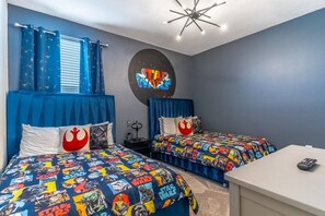 A bedroom with two beds, each with Star Wars themed bedding, a Star Wars poster on the wall, and a modern ceiling light fixture.