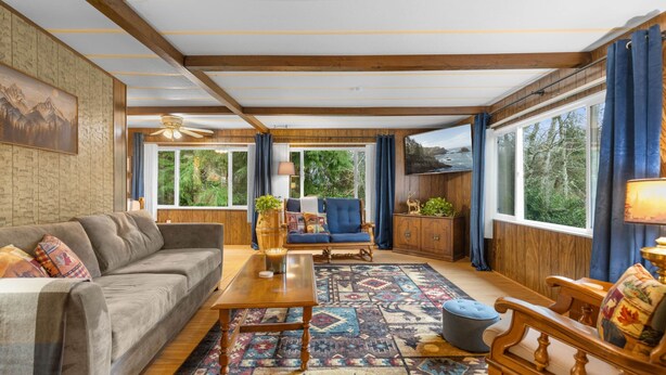A spacious living room with a sofa, a coffee table, a blue armchair, and a patterned rug. - Forest Cabin Near Sekiu Fish & Hunt Basecamp (Clallam County)