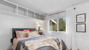 A bedroom with a bed, a nightstand, a lamp, and a window with curtains. - Forest Cabin Near Sekiu Fish & Hunt Basecamp (Clallam County)