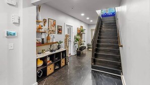 Un interior moderno con una escalera, un pasillo con estanterías y una puerta que da a otra habitación.
