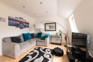 A modern living room with a grey sofa, teal cushions, a black and white rug, a TV, a lamp, and a world map on the wall. - Cosy London Apartment Near River Thames (London)