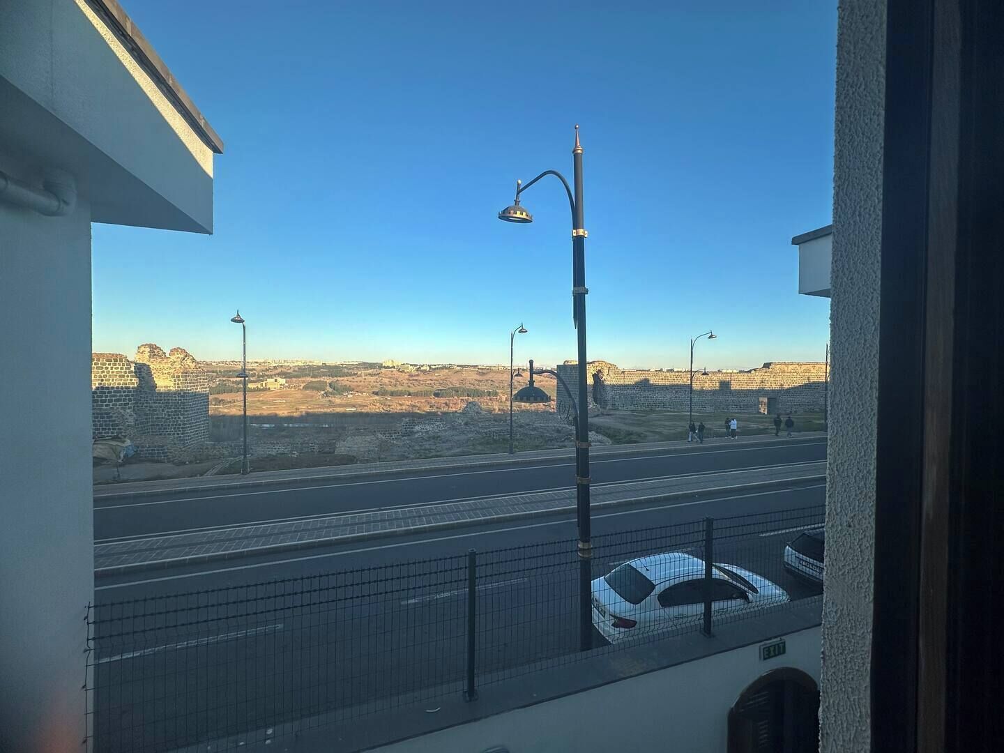 Une vue depuis un balcon donnant sur une route bordée d’un mur en pierre et d’éclairages publics.