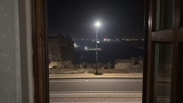 Una vista notturna da una finestra, con una strada, un muro in mattoni e un lampione.