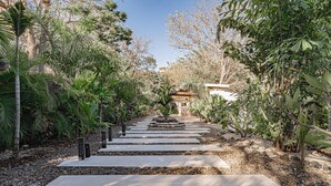 Un camí de jardí amb lloses de pedra i pedres, envoltat de diverses plantes tropicals.