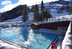 Ein Schwimmbad mit einer Holzhütte und einer Seilbahn im Hintergrund.