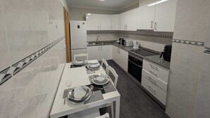 A modern kitchen with white cabinets, a granite countertop, and a dining table set for four. - Patio do garajau (Caniço)