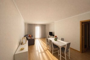 Eine moderne Wohnung mit Essbereich, Wohnzimmer mit Sofa und Fernseher sowie ein großes Fenster mit Vorhängen.