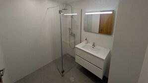 A modern bathroom with a glass shower enclosure, a white sink with a mirror above it, and a light fixture on the ceiling. - Patio do garajau (Caniço)