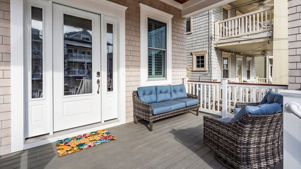 A covered porch with wicker furniture, a white door, and a small balcony. - Brand new, beach block, 3bedroom 2 bath duplex! (Ocean City)