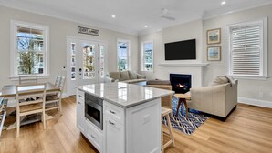 A modern kitchen with a central island, a dining area with wooden chairs, a living room with a sofa and a fireplace, and large windows with blinds. - Brand new, beach block, 3bedroom 2 bath duplex! (Ocean City)