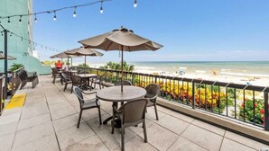 An outdoor patio with round tables and chairs, umbrellas, and a view of the beach. - Compass Cove Condo 256 (Myrtle Beach)