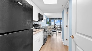 A kitchen with white cabinets, a black refrigerator, and a dining area with a table and chairs. - Compass Cove Condo 256 (Myrtle Beach)