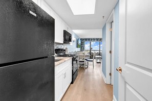A kitchen with white cabinets, a black refrigerator, and a dining area with a table and chairs. - Compass Cove Condo 256 (Myrtle Beach)