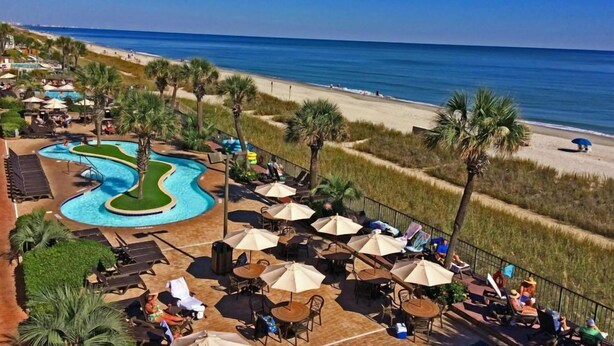 A resort with a swimming pool, beach, and outdoor seating area. - Compass Cove Condo 256 (Myrtle Beach)