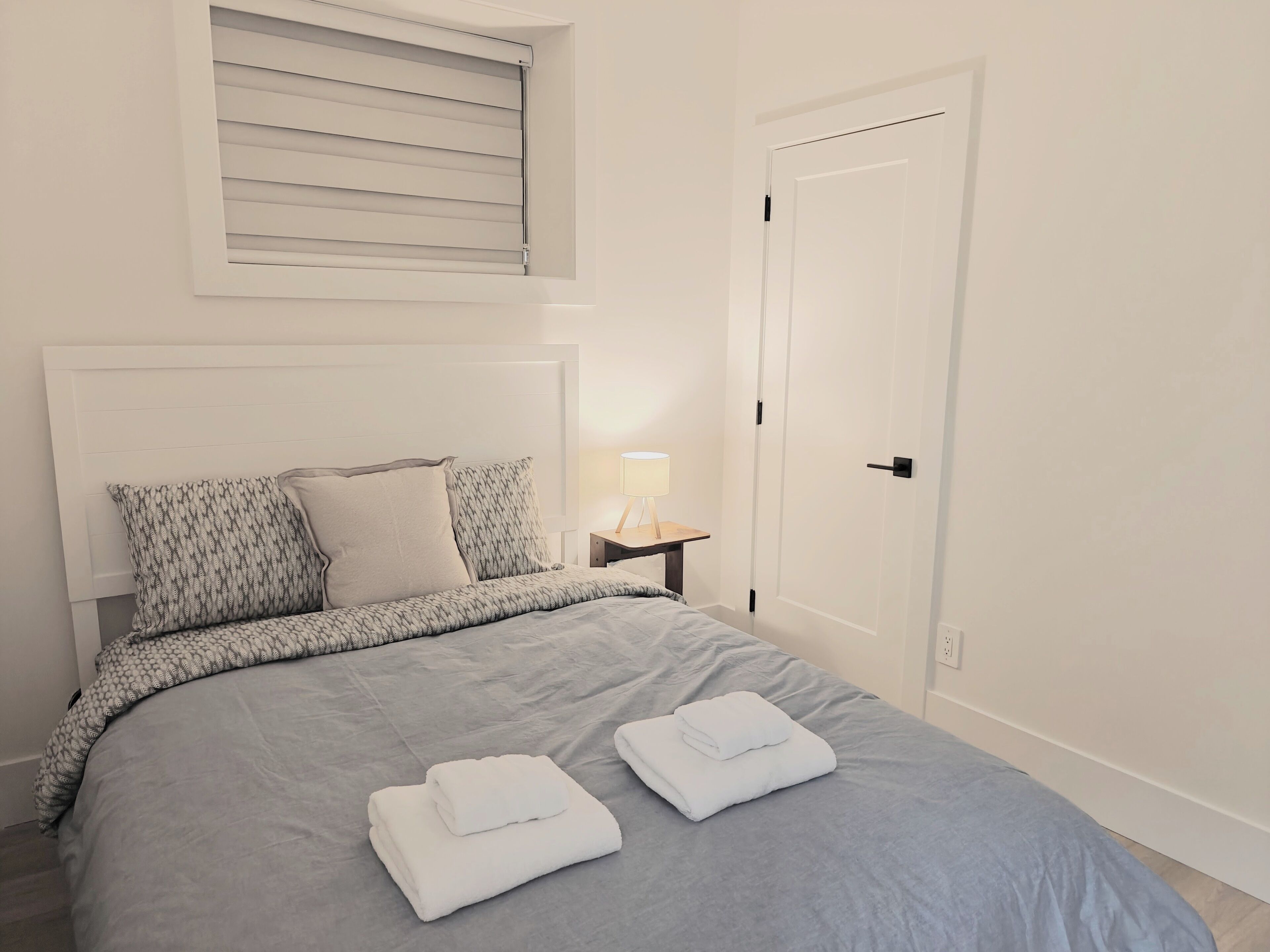 A neatly made bed with a grey bedspread and two folded white towels.