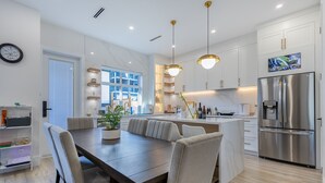 A modern kitchen with a central island, stainless steel appliances, and a dining area with a large table and chairs. - 5 BR Brand New Luxurious White Rock Spacious Home (Surrey)