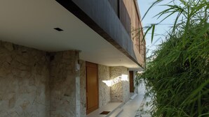 A modern building with a stone facade, wooden balconies, and a pathway lined with white pebbles and green plants. - Ultra-Luxe 4BR Seminyak Villa | Enclosed AC Living & Private Pool (Seminyak)