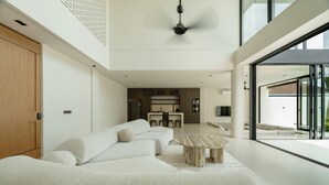 A modern living room with a sofa, a coffee table, and a view of the kitchen and outdoor area. - Ultra-Luxe 4BR Seminyak Villa | Enclosed AC Living & Private Pool (Seminyak)