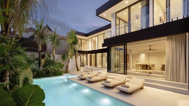 A modern house with a swimming pool, lounge chairs, and a well-lit interior. - Ultra-Luxe 4BR Seminyak Villa | Enclosed AC Living & Private Pool (Seminyak)