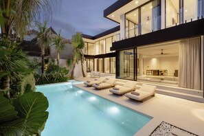 Una casa moderna con piscina, sillas de descanso y un interior bien iluminado.