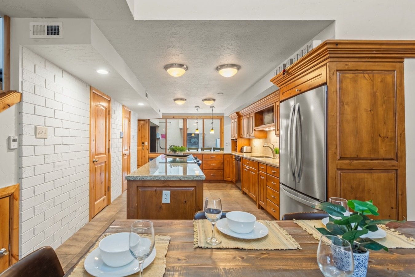 A modern kitchen with wooden cabinets, a stainless steel refrigerator, and a dining area set for a meal.