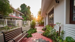 A narrow pathway with a bench and potted plants, leading to a building with large windows and a white exterior. - Anjaneyam 4BHK Heritage Villa - Near Marine Drive (Kochi)