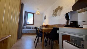Tunnelmallinen huone, jossa on puinen ruokapöytä, tuoleja, sohva ja pieni keittiönurkkaus, jossa on kahvinkeitin.