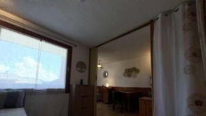 Kodikas olohuone, jossa on sohva, ruokailutila pöytineen ja tuoleineen sekä keittiö, jossa on kaappeja.