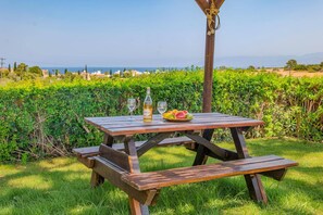 A wooden picnic table with a bottle and glasses, surrounded by greenery and a view of the sea. - Villa Akamas Bayview by Villa Plus (Latchi)