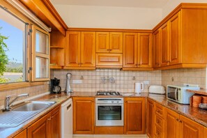 A kitchen with wooden cabinets, a stainless steel sink, a coffee maker, a toaster, and an oven. - Villa Akamas Bayview by Villa Plus (Latchi)