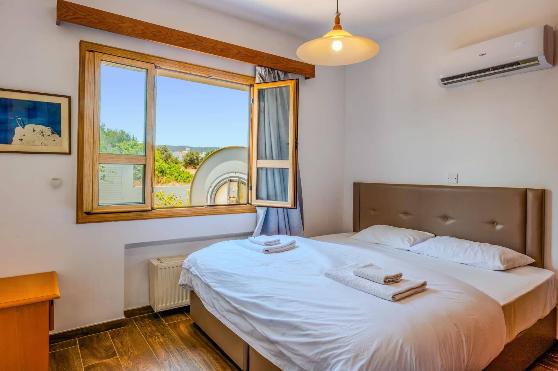A bedroom with a large bed, a window with curtains, a radiator, and an air conditioning unit.